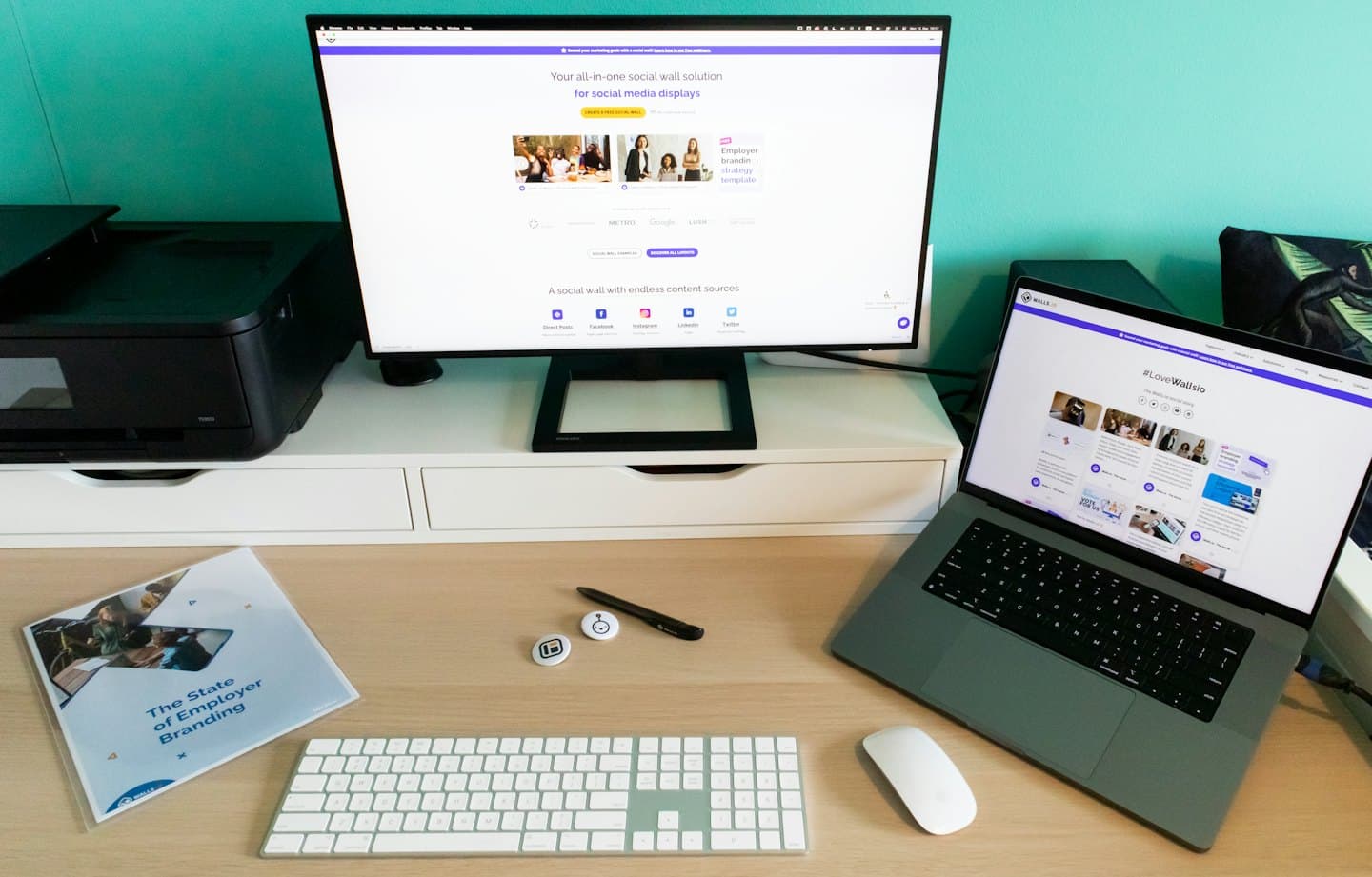 Bilgisayar monitörleri ve işveren markalama materyallerinin bulunduğu modern ofis masası.